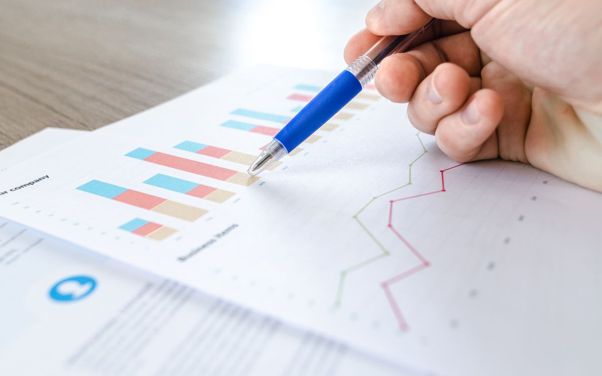 A hand holding a pen over printed bar charts and line graphs
