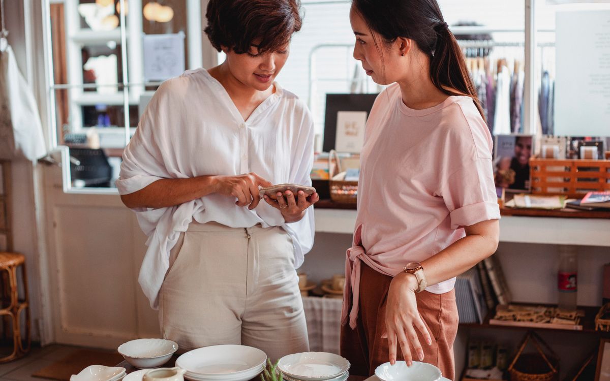 Two shoppers consulting a smartphone while browsing ceramics in a shop