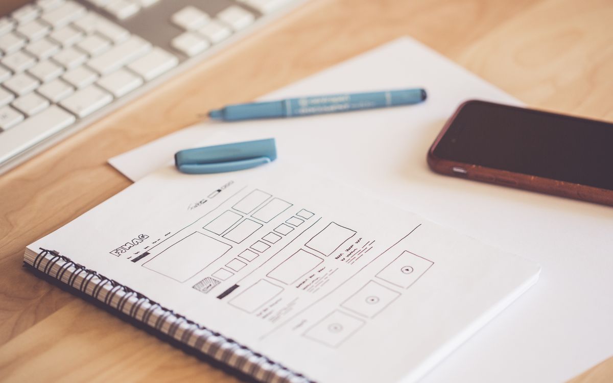 Hand-drawn website wireframes in a notebook beside a phone and keyboard